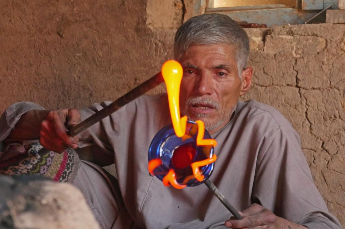 An elderly Afghan artisan shaping molten red glass on a blowpipe in a traditional workshop in Herat.