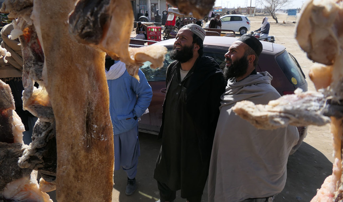 Local tribesmen standing near hanging dried lamb meat at a roadside butcher shop in Pishin Balochistan