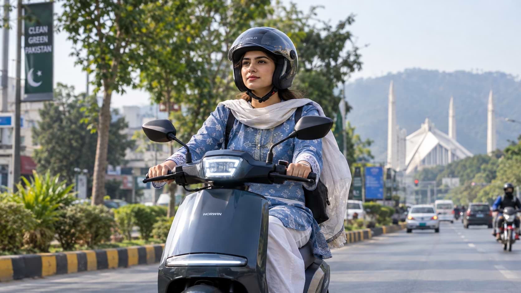 Pakistani woman in a helmet riding an electric scooty on an Islamabad avenue with Faisal Mosque in the background.