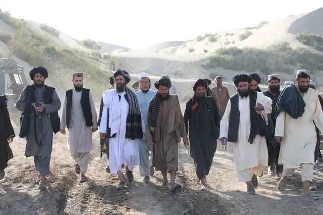 Taliban government officials and delegates walking along a dirt pathway near a construction site in northern Afghanistan