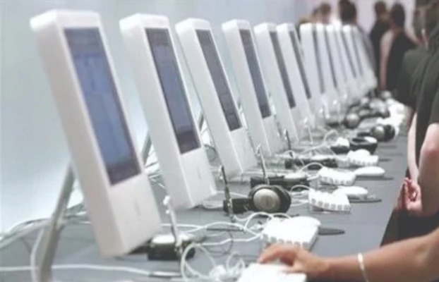 A row of white desktop computer workstations with headphones and keyboards set up in a digital training lab.